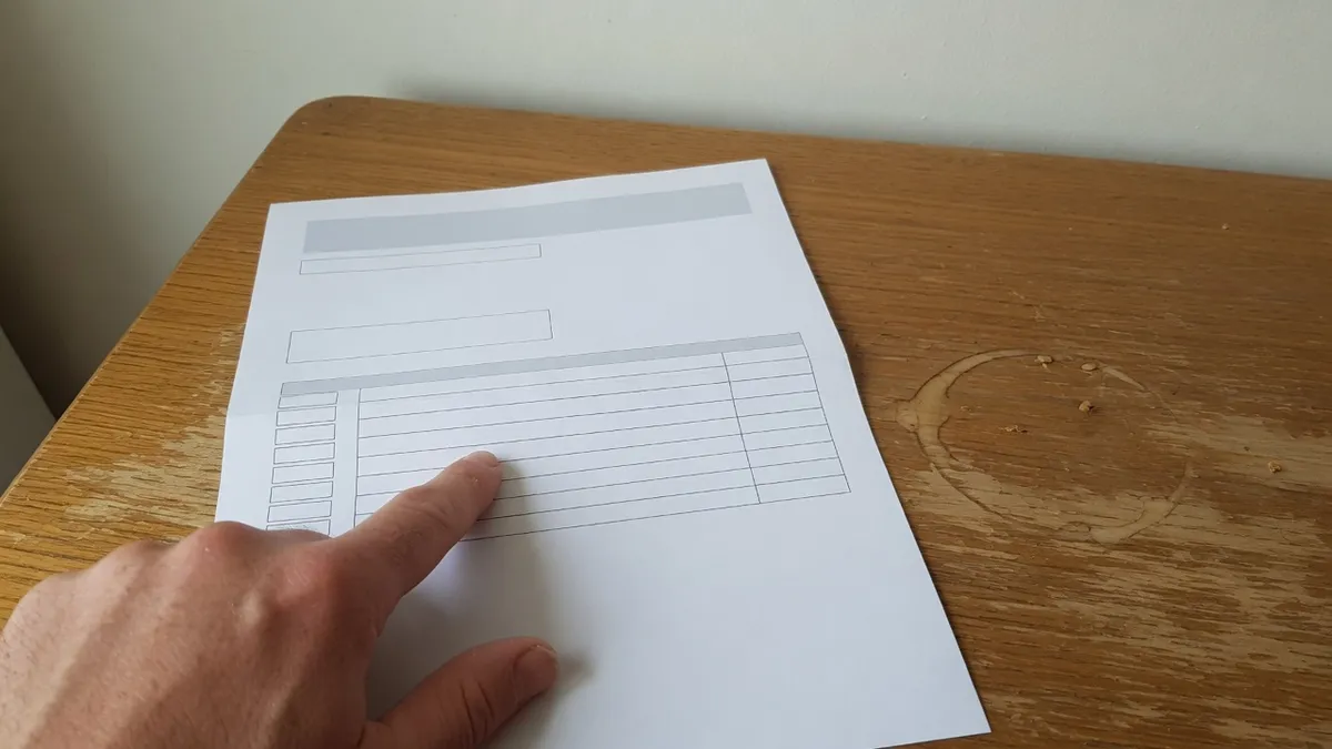 A hand on a kitchen table with the index finger pointing at one ruled line on a blank mortgage statement form, its boxes and columns empty